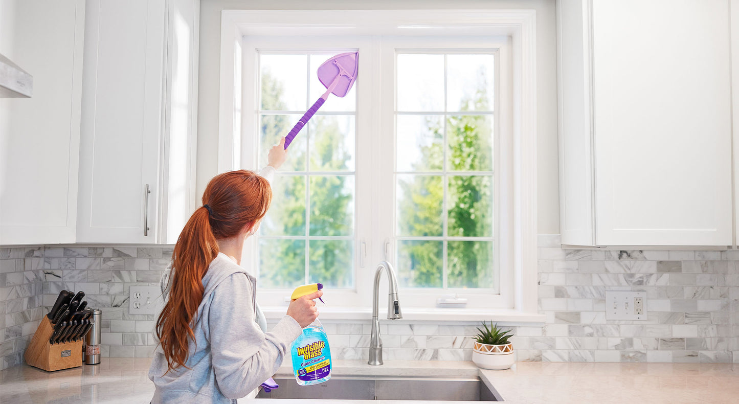 Woman cleaning kitchen window with Invisible Glass Cleaner and Reach & Clean tool